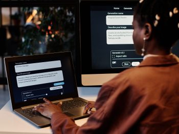 Laptop screen with AI generating task and rear view of young African American female designer pressing keys of keyboard