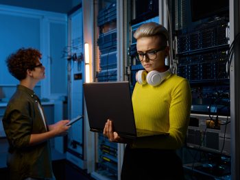 Serious technicians working together with network hardware in dark server room of modern business data center with supercomputer