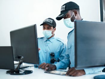 Shot of two masked young security guards on duty at the front desk of an office.